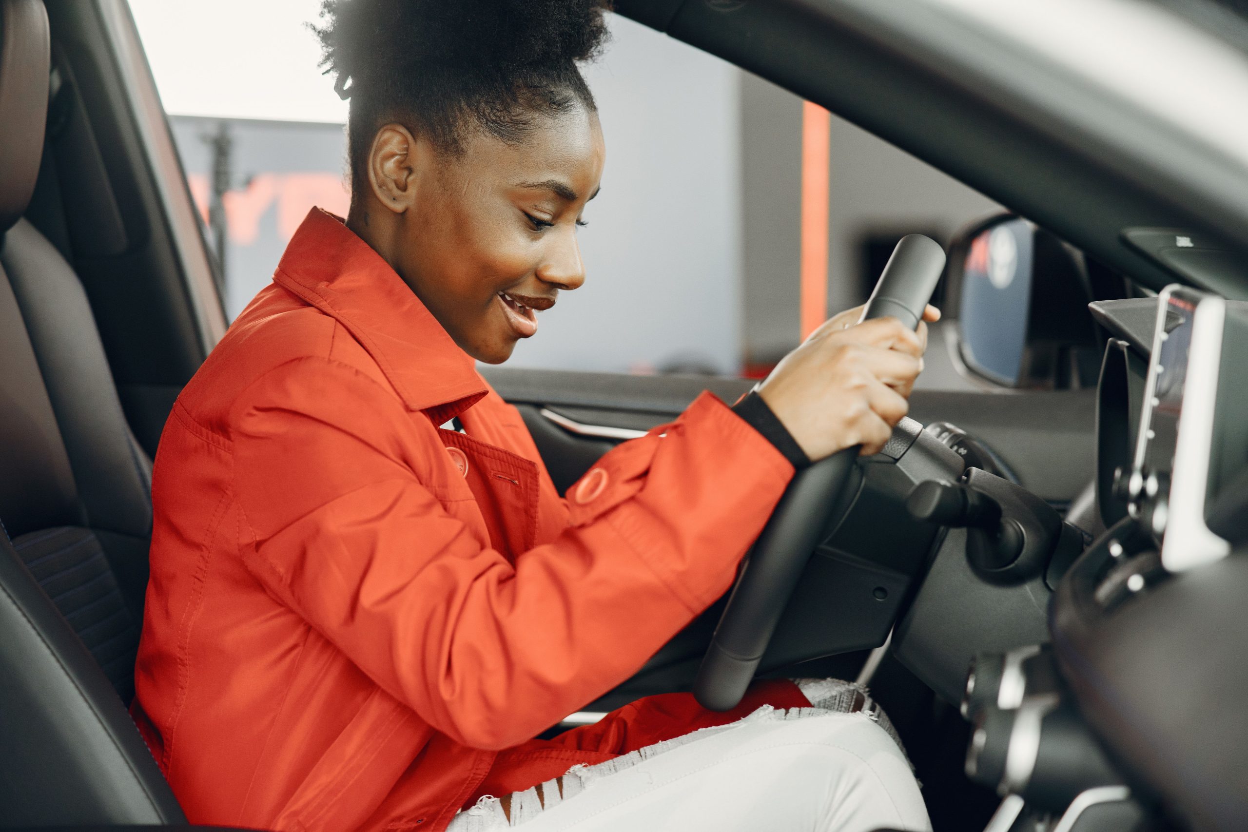 Jeune femme en veste orange essayant volant voiture enthousiaste